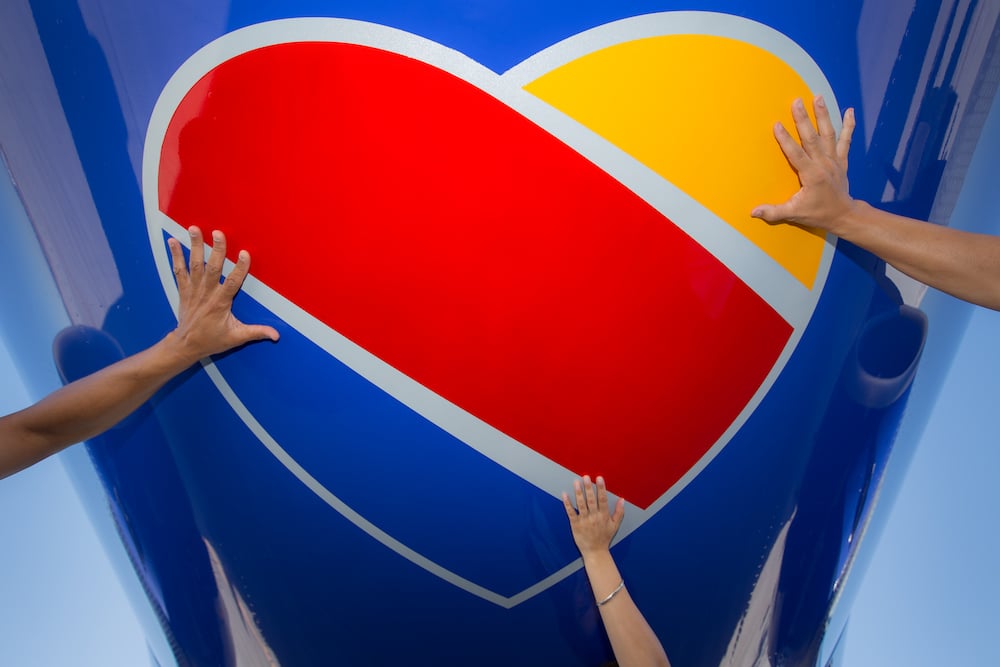Multiple hands touching large red and yellow heart-shaped logo on blue aircraft fuselage