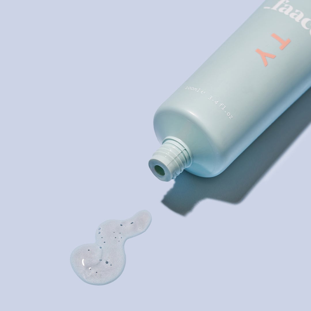 Light blue bottle with coral text dispensing white exfoliating gel onto gray surface