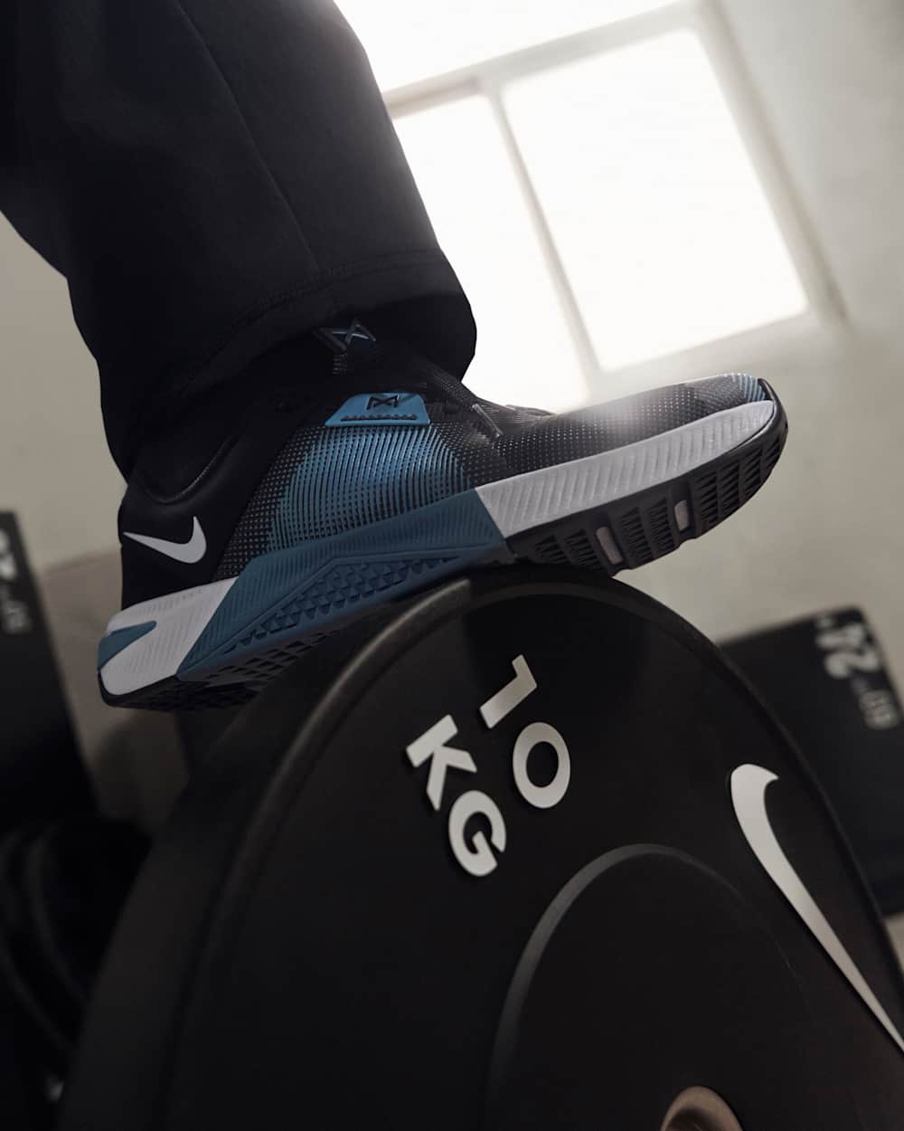 Person wearing black athletic shoe with blue and white accents, standing on KG-branded equipment
