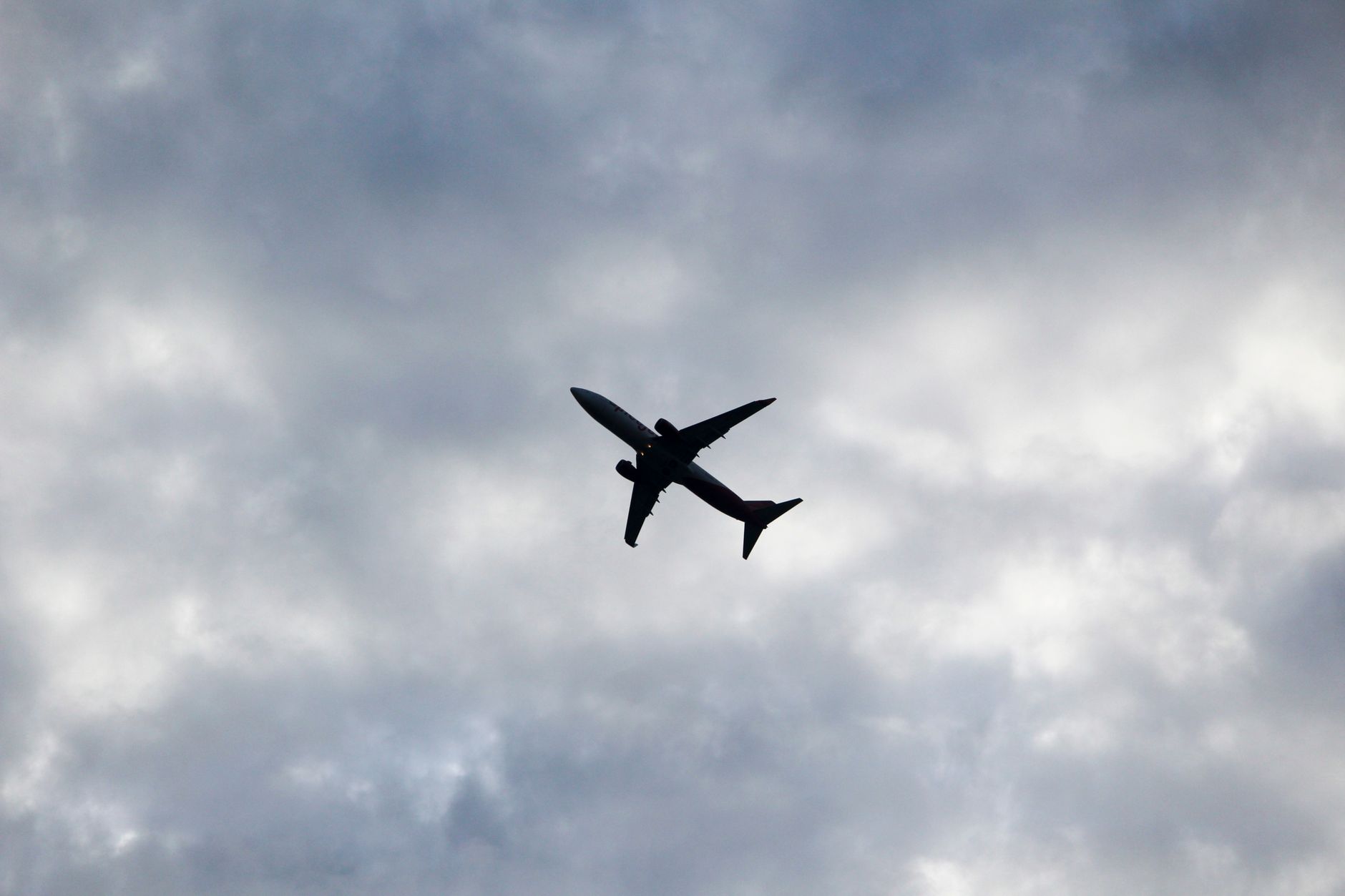 Silhouette of a commercial aircraft flying against a cloudy gray sky