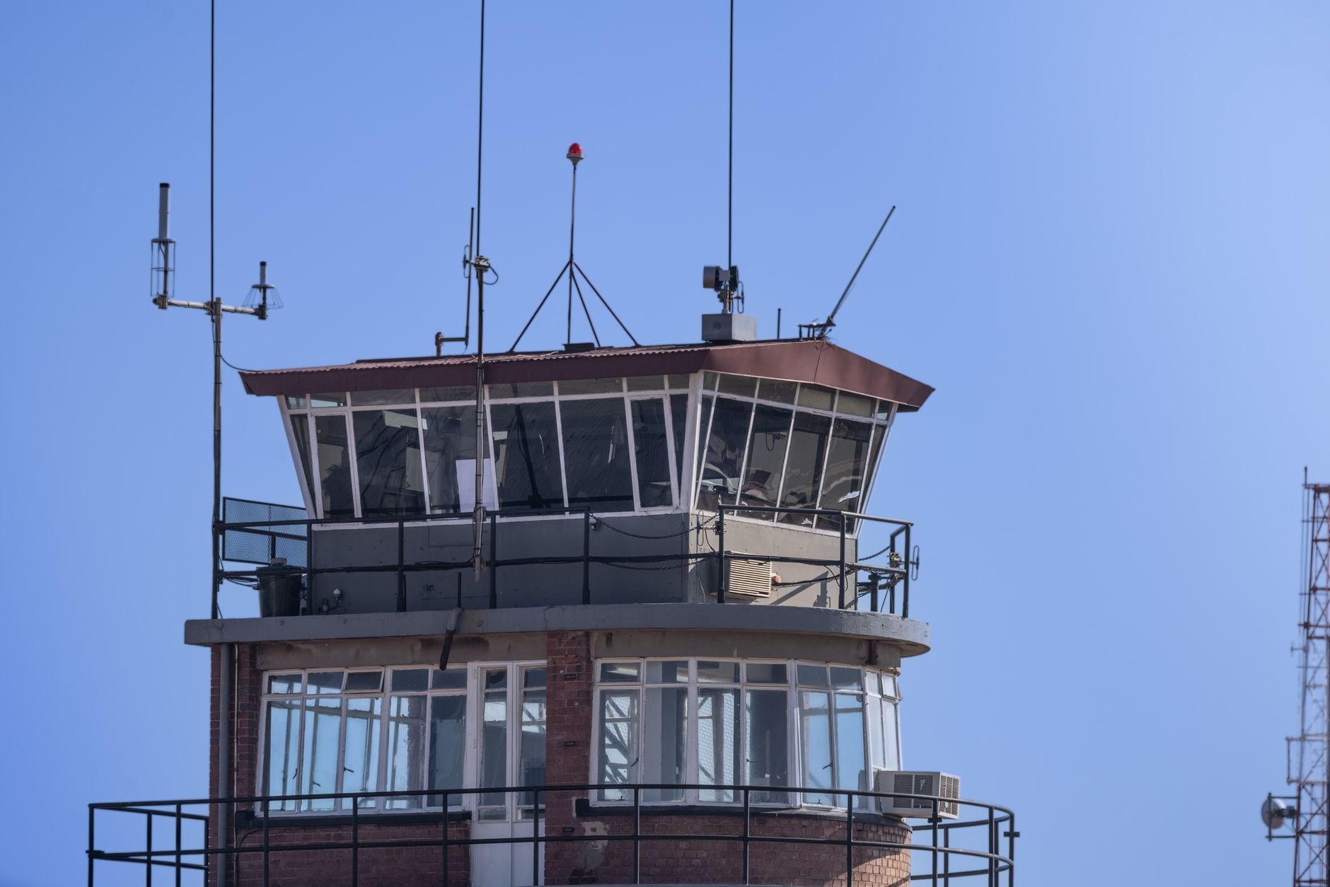 Air traffic control tower with red brick base, glass upper levels, and antennas against clear blue sky