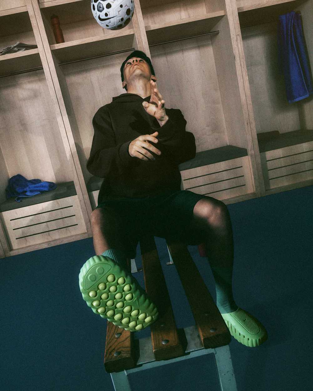 Man in black jacket in locker room tossing soccer ball upward