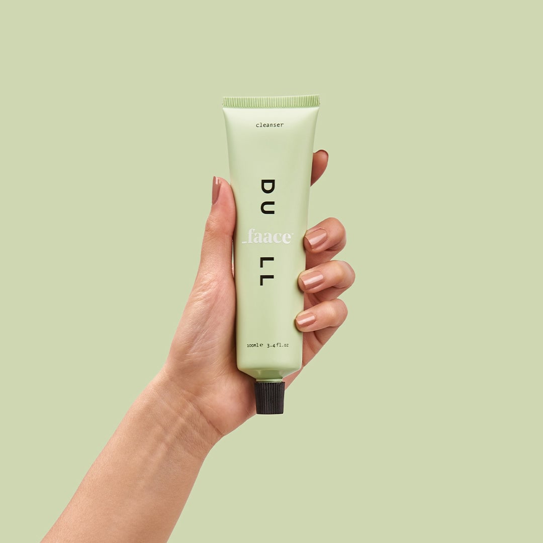 Person holding pale green cleanser tube against matching background