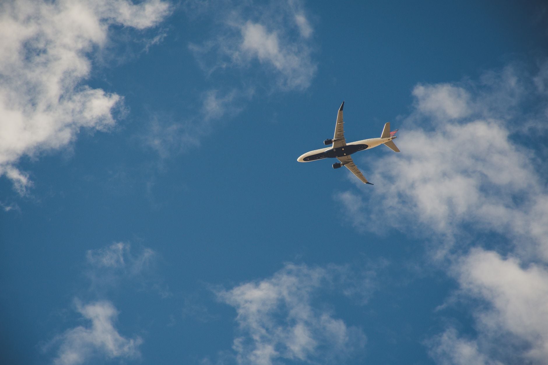 White and tan commercial aircraft in flight against a blue sky with white clouds