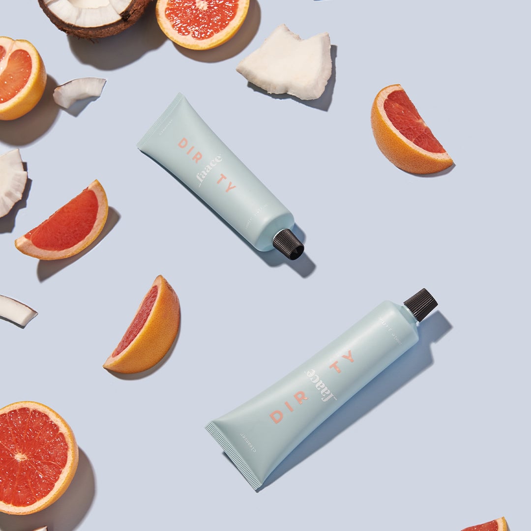 Two light blue skincare tubes surrounded by grapefruit halves and coconut pieces
