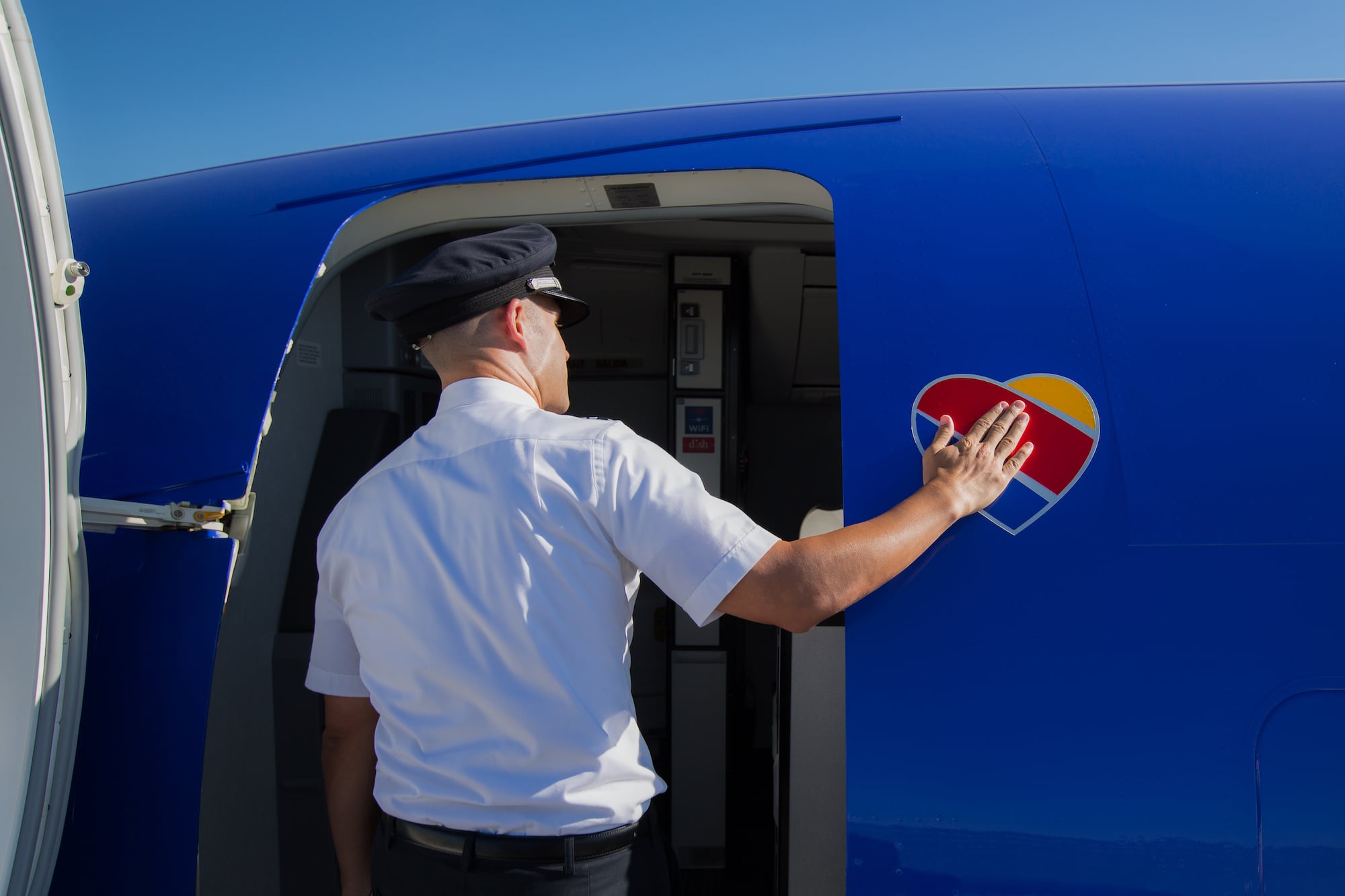 Pilot in uniform applying heart-shaped logo decal to blue aircraft exterior